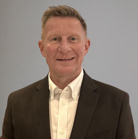 A man in a suit smiling against a plain background.