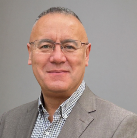Smiling man in a grey suit with glasses and short, grey hair against a neutral background.
